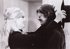 an old black and white photo of a woman helping a man fix his hair in front of a mirror