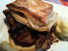 a white plate topped with meat and pastry next to mashed potatoes on a table