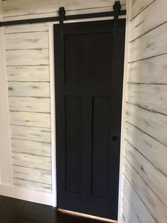 an empty room with a black door and white sidings on the wall behind it