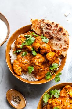 two bowls filled with chicken curry and rice next to pita bread on a table