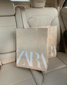 two shopping bags sitting on the back seat of a car, next to a bag that says zara