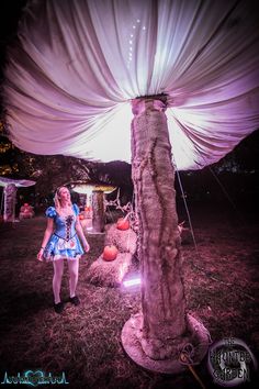 a woman standing next to a tall tree in the middle of a field at night