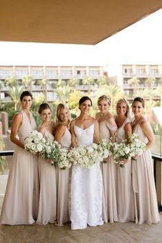 a group of women standing next to each other in front of a building holding bouquets