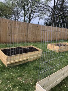 two wooden raised beds with plants in them on the grass next to a wood fence