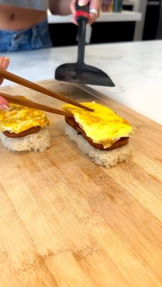 someone holding chopsticks over some food on a cutting board with another person in the background