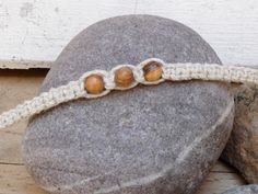 three beads on a white crochet bracelet sitting on top of a rock next to some rocks