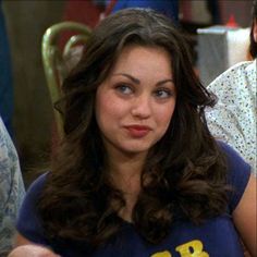 a woman sitting at a table with a plate of food in front of her and two other people behind her