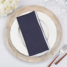 a place setting with napkins, silverware and white flowers on the tablecloth