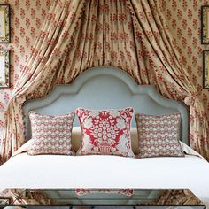 a bed with four pillows on top of it in front of a curtained wall