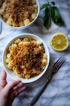 two bowls filled with macaroni and cheese on top of a marble table next to silverware