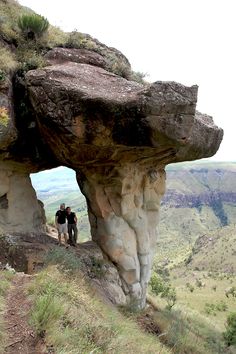 two people are standing at the top of a cliff looking out into the valley below