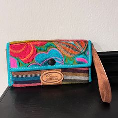 a multicolored purse sitting on top of a black table next to a white wall