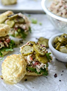 a sandwich with pickles, cheese and other toppings next to a bowl of pickles