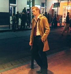 a man in a trench coat and tie standing on the side of a street at night