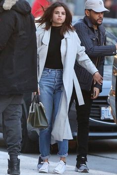 a man and woman walking down the street with one holding onto her hand while another walks behind them