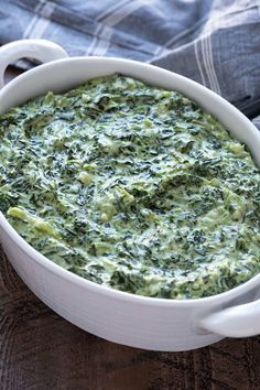 a white bowl filled with spinach on top of a wooden table next to a napkin