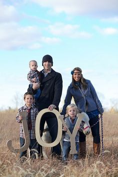 a family posing for a photo in a field with the word joy spelled by two large letters