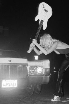 a woman is playing an electric guitar in front of a car