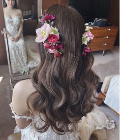 a woman sitting in front of a mirror with flowers in her hair