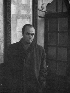 a black and white photo of a man standing in front of a window