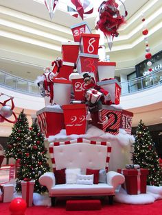 a large christmas tree in the middle of a shopping mall with presents on it's sides