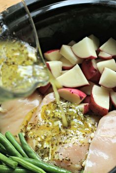 someone pouring sauce on some food in a crock pot with potatoes and green beans