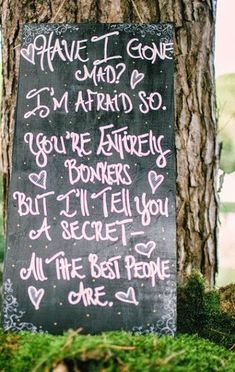 a chalkboard sign with writing on it next to a tree in the grass,