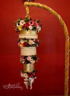 a wedding cake with flowers on it is hanging from a gold ribbon in front of a red wall