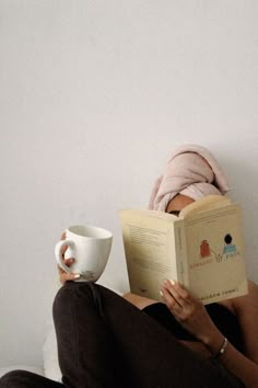 a woman reading a book while holding a coffee cup