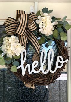 a wreath with the word hello painted on it and some flowers hanging from the front door