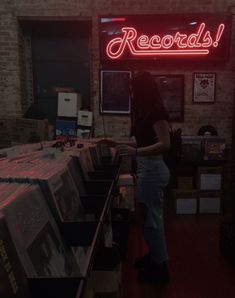 a woman standing in front of a record store with records on the counter and neon sign above her