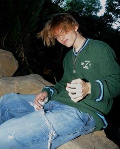 a young man sitting on top of a rock