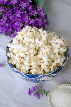 a blue and white bowl filled with popcorn next to some purple flowers on a table