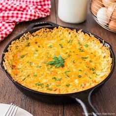 an omelet in a cast iron skillet on a wooden table with eggs and milk