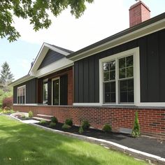 a house with black siding and white trim on the windows, grass in front of it