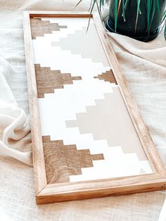 a wooden frame with a white and brown pattern on it next to a potted plant