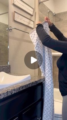 a woman is holding up a towel in front of a bathroom sink and shower stall