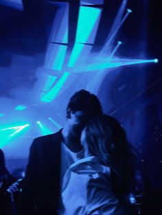 a man and woman standing next to each other in front of blue lights at a concert