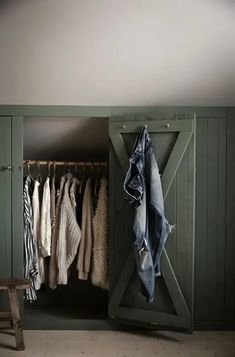 an open closet with clothes hanging on hangers and a bench in front of it