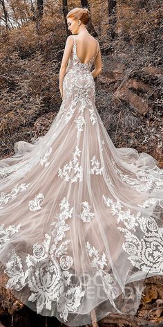 a woman standing in the woods wearing a wedding dress with white flowers and lace on it