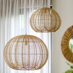 two rattan lamps hanging from the ceiling next to a plant in front of a window