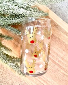 a glass with reindeers painted on it sitting next to a pine tree