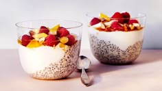 two bowls filled with fruit and yogurt on top of a white table next to a spoon