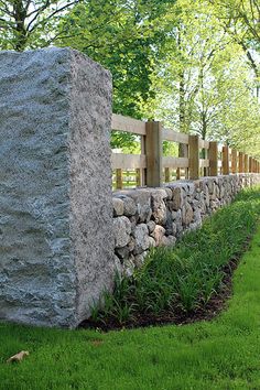 a stone wall with grass and trees in the background