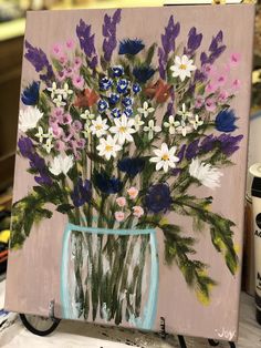 a painting of flowers in a vase on a table next to paintbrushes and paints