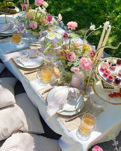 an outdoor table set up with flowers and desserts