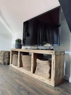 a flat screen tv sitting on top of a wooden shelf next to baskets and a plant