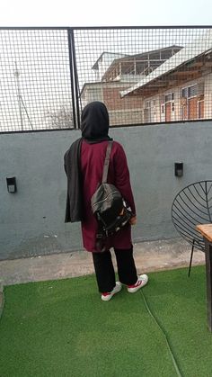 a person in a red jacket and black backpack is standing on the grass near a table