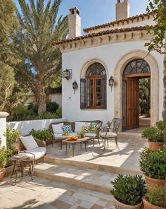 a patio with chairs, tables and potted plants on the side of the house