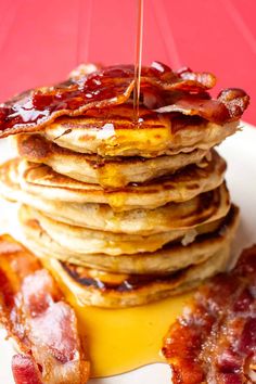 stack of pancakes with bacon and syrup being drizzled on top